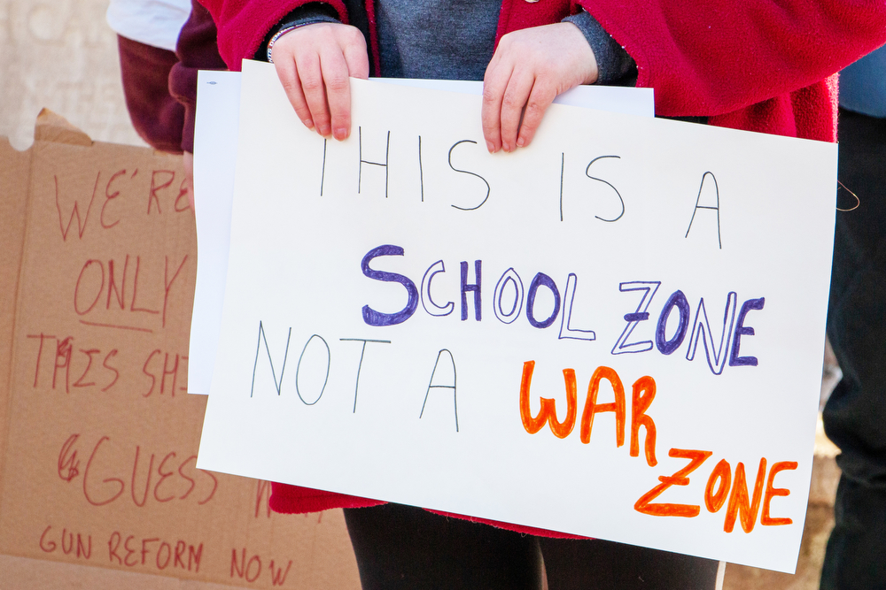 一名集会参与者举着一个牌子，上面写着:“这里是学校，不是战区。”